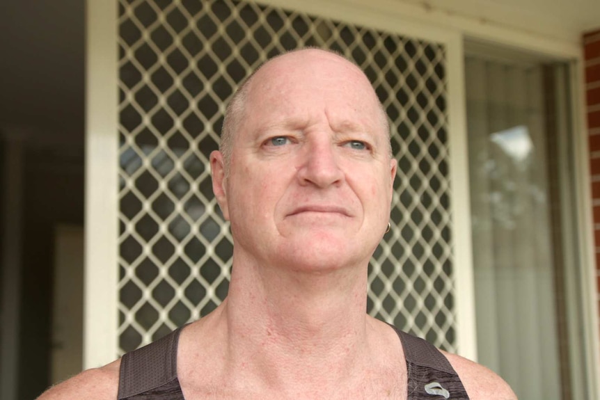 A man wearing a singlet top stands in front of a screen door.