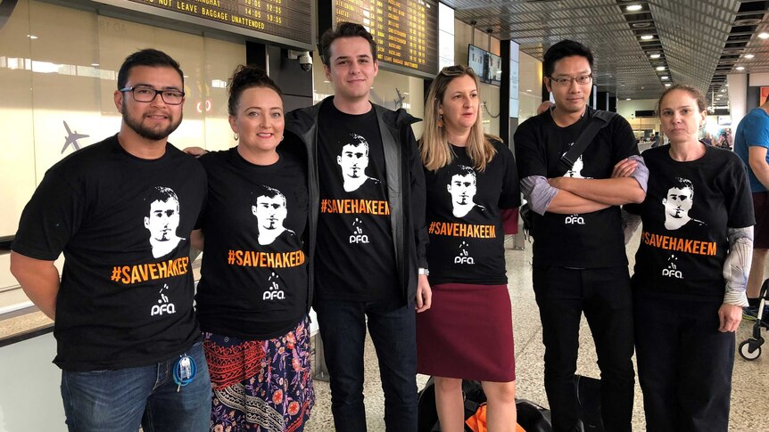 Five people wearing black shirts with the words 'save Hakeem', standing in front of an airport flight board