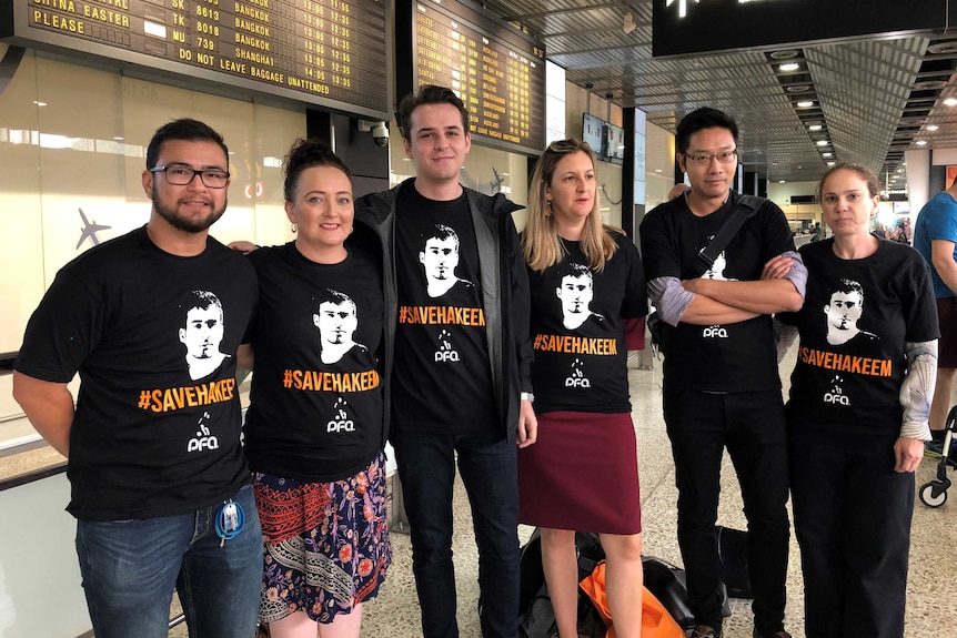Five people wearing black shirts with the words 'save Hakeem', standing in front of an airport flight board