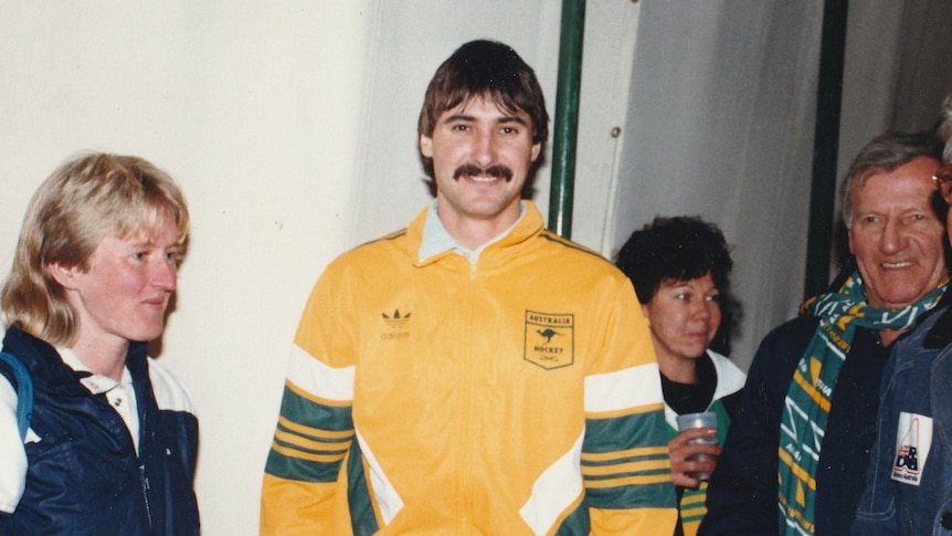 Man in yellow jumper smiles at camera while surrounded by people