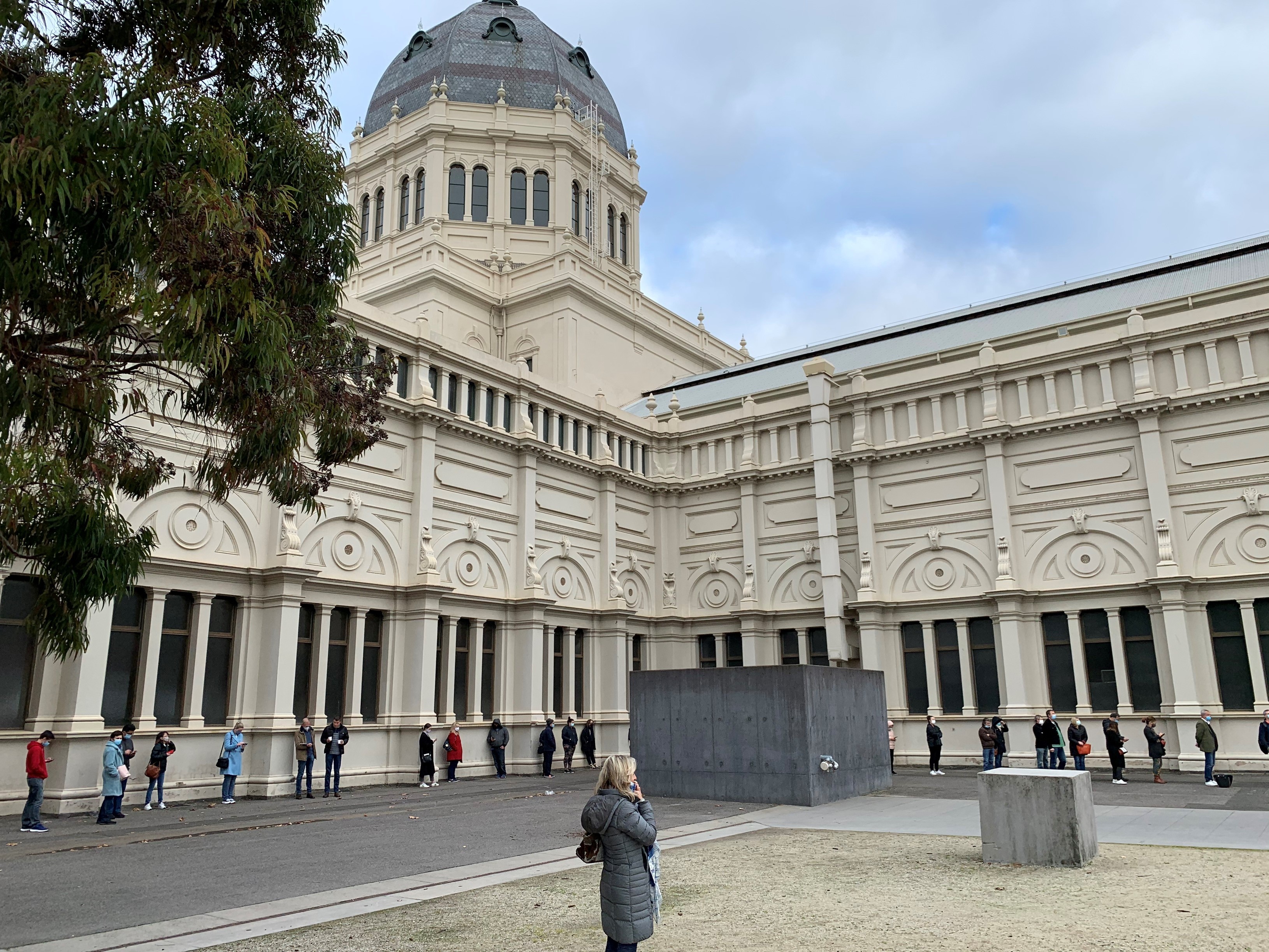 People are standing about 1.5m apart in a line that stretches around a large building.