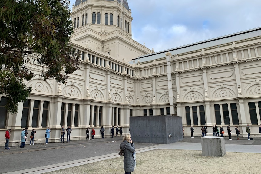 People are standing about 1.5m apart in a line that stretches around a large building.