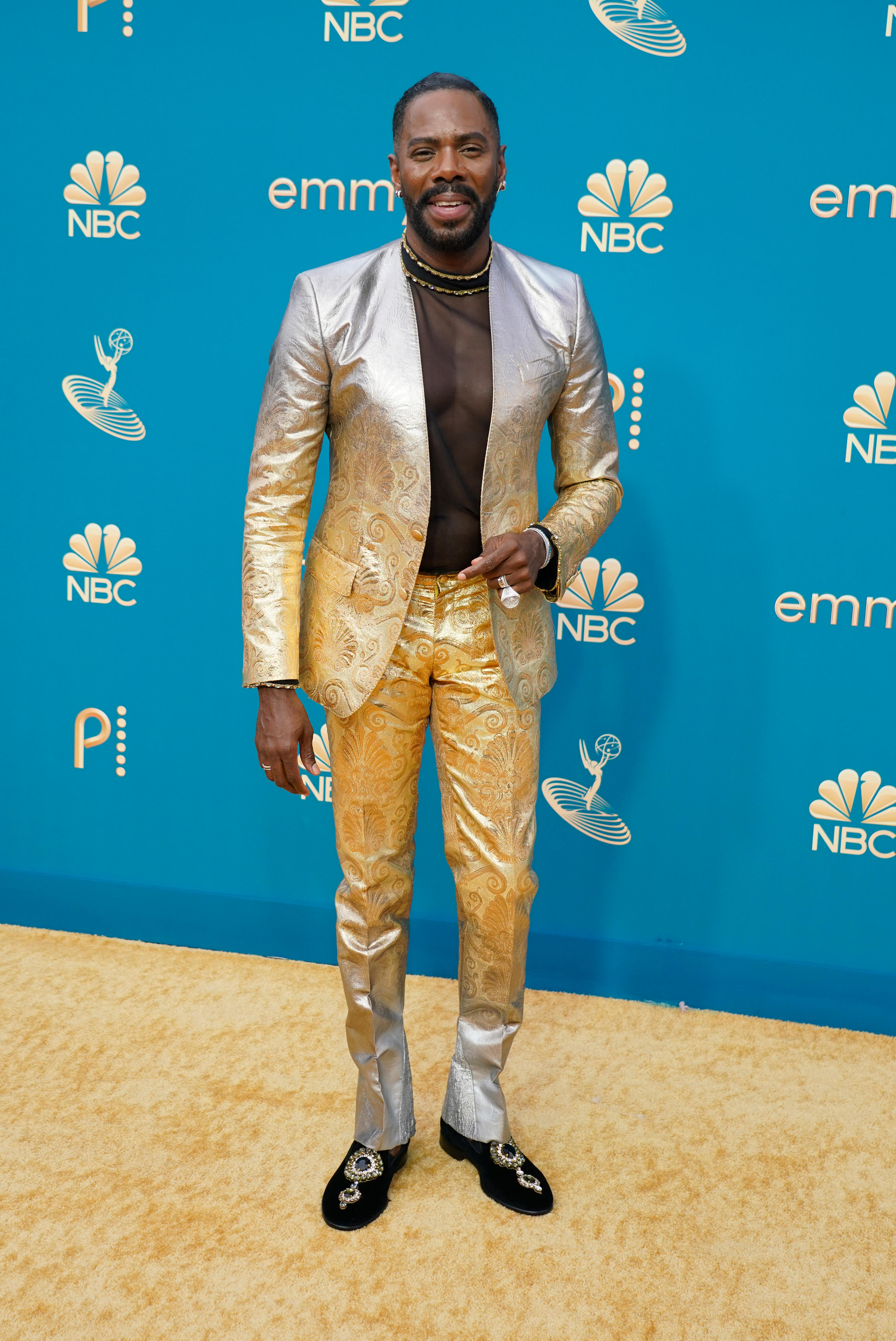Colman Domingo wearing a gold metallic suit with a black sheer mesh shirt underneath. 