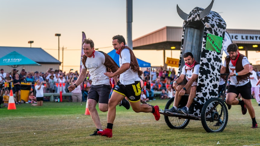 Four men running with a a cow-themed portaloo