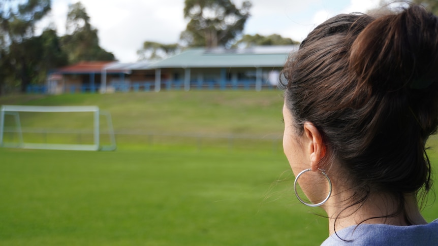 A woman looks across a soccer ground towards a set of changerooms set up on a hill