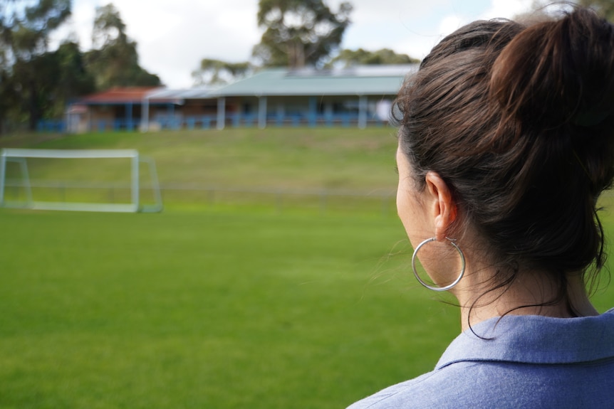 Une femme regarde à travers un terrain de football vers un ensemble de vestiaires sur une colline