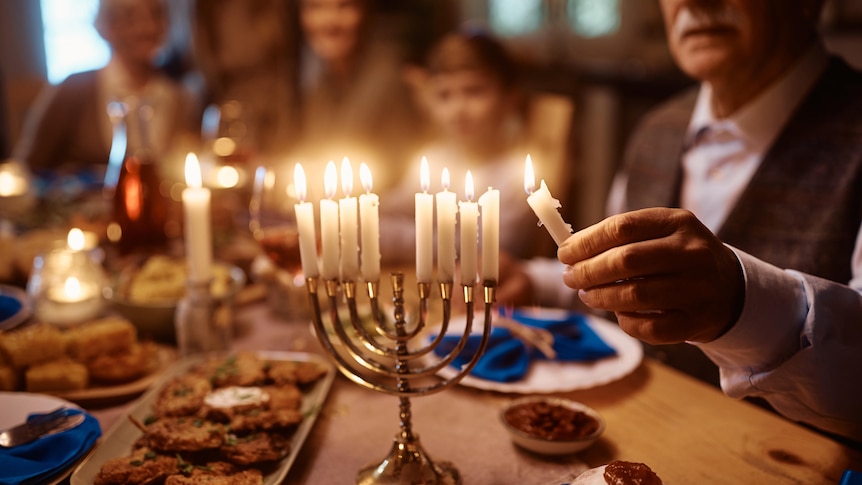 A man lights a menorah, which sits on a table covered with plates of food.
