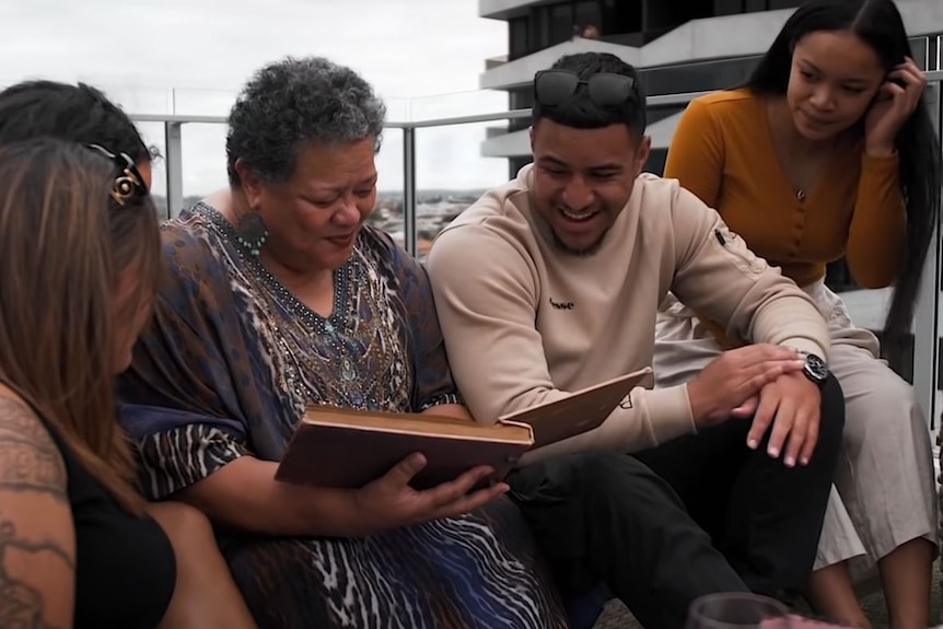 A woman holds a photo album she is surrounded by five family members. 