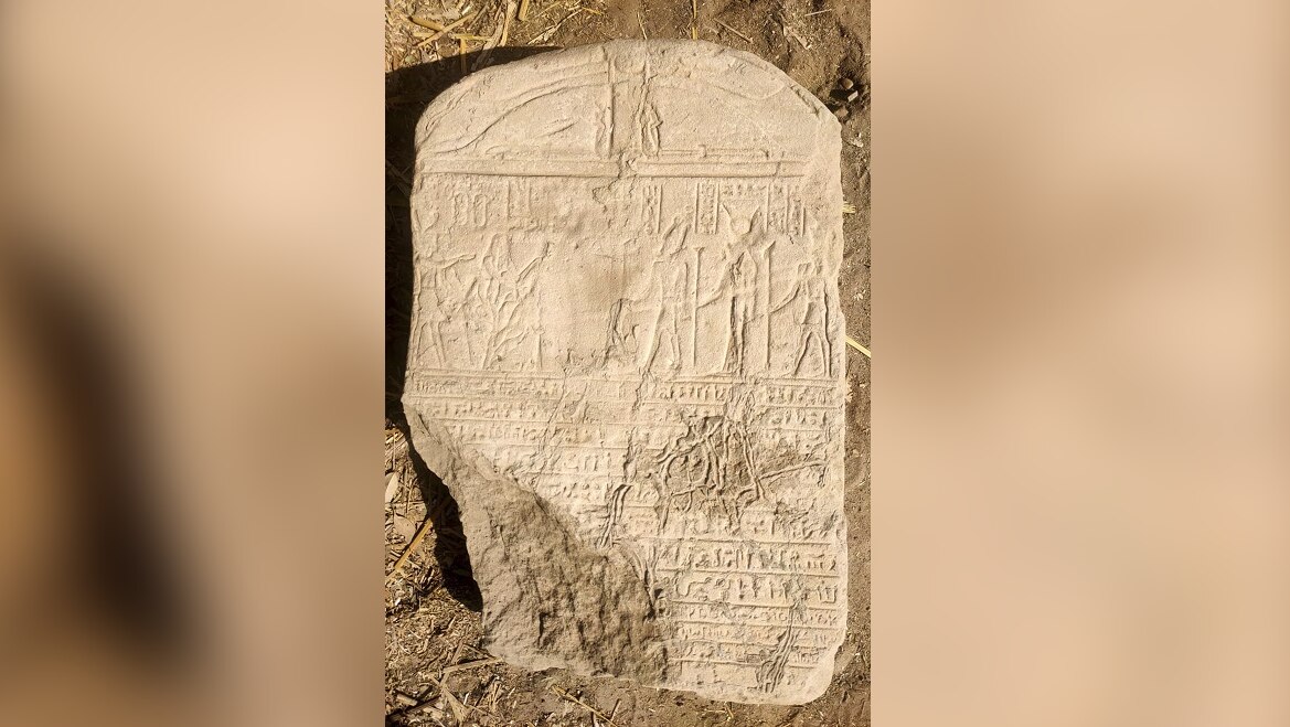 A beige stone tablet covered in hieroglyphics and ancient writings sits on the ground.