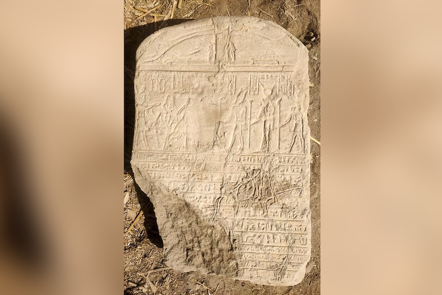 A beige stone tablet covered in hieroglyphics and ancient writings sits on the ground.