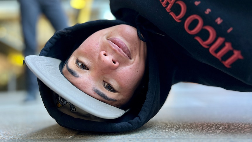 A breakdancer looks at the camera while upside down