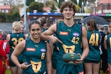 A  young woman and man in football uniforms smile at the camera