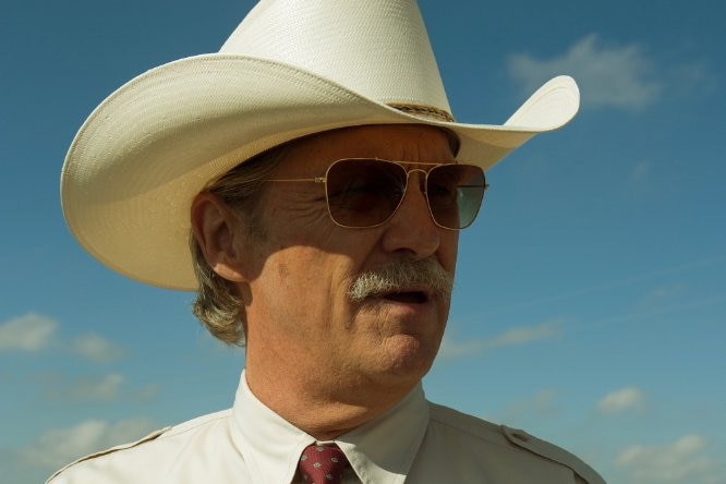 Jeff Bridges, wearing a broad cowboy hat, aviator glasses and full moustache, in a scene from Hell or High Water.