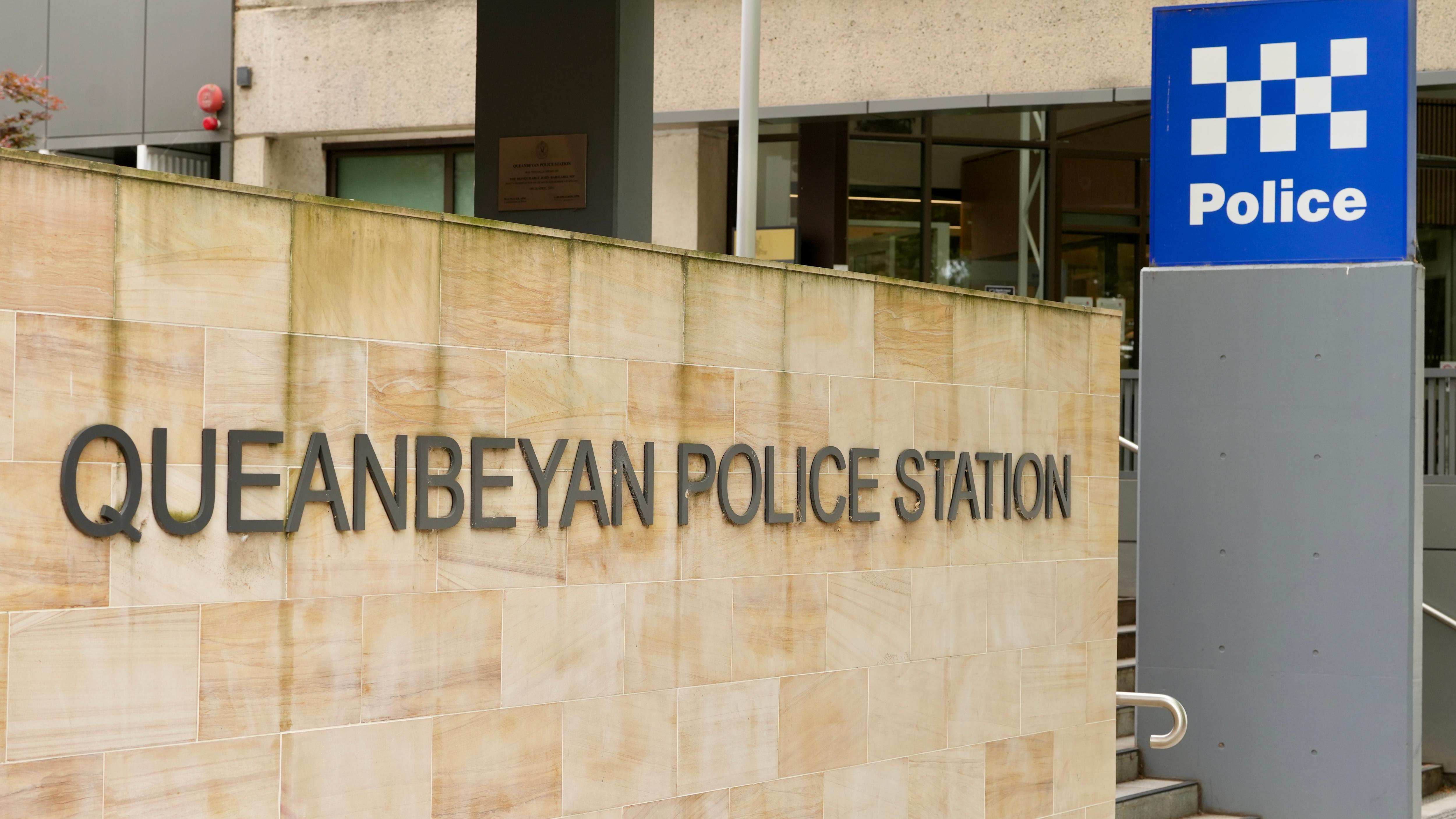 Uma parede de pedra traz as palavras Delegacia de Polícia de Queanbeyan e polícia está escrita em azul em uma placa separada.