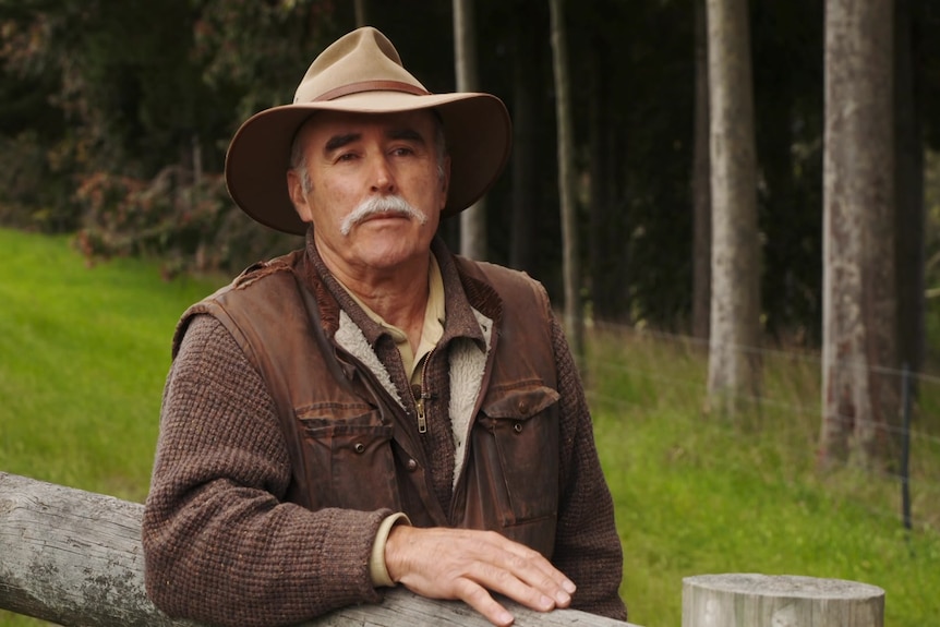 Photo of a man wearing a hat leaning over a fence.