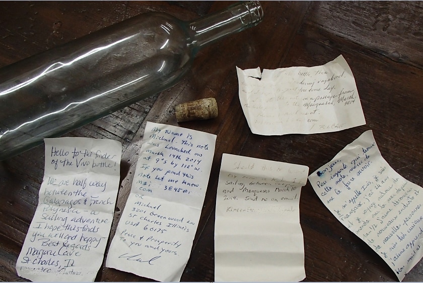 Five sun bleached notes written in English and French and the glass bottle they were found in.