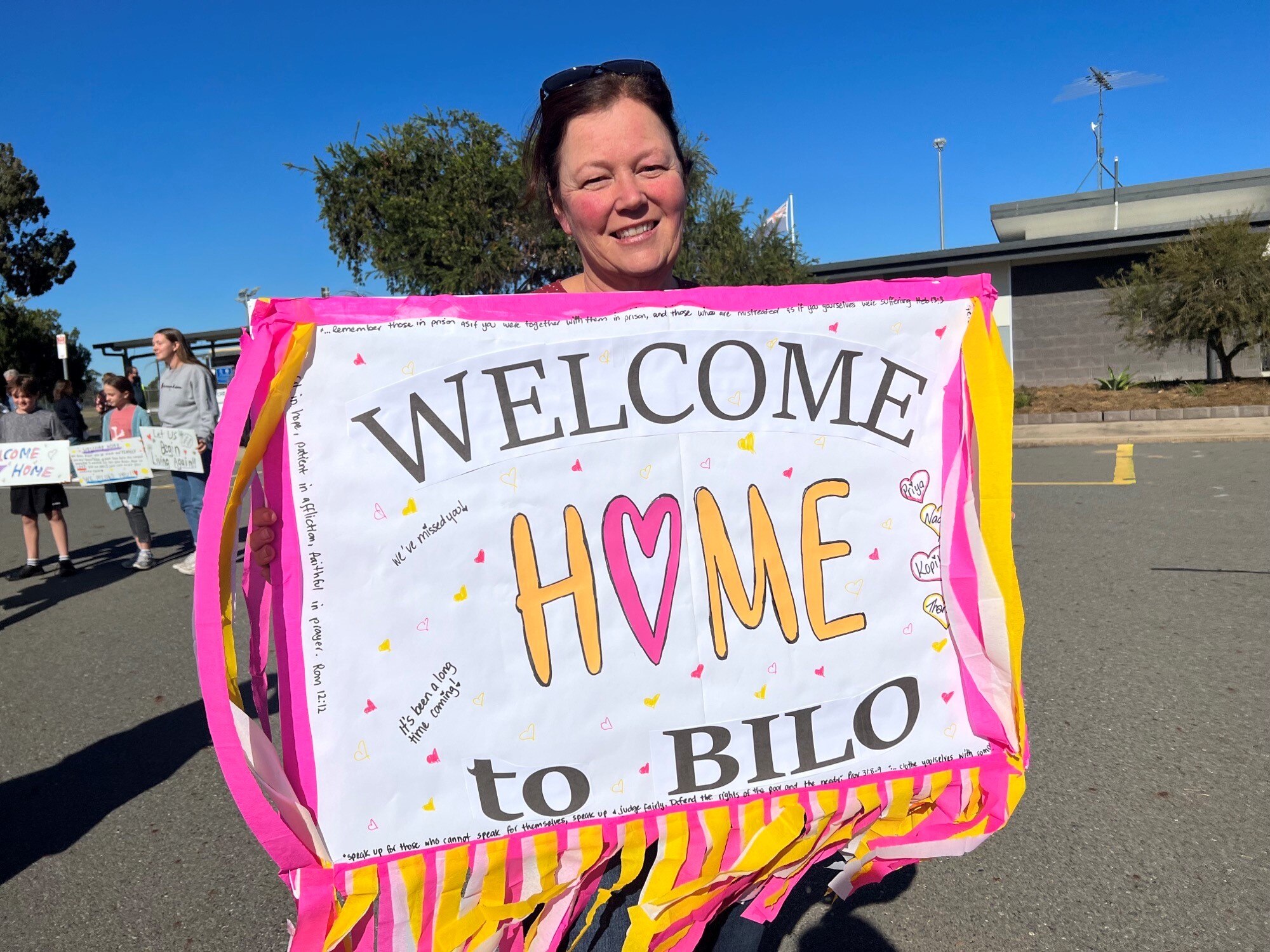 A smiling woman holding a large "welcome" sign at an airport.