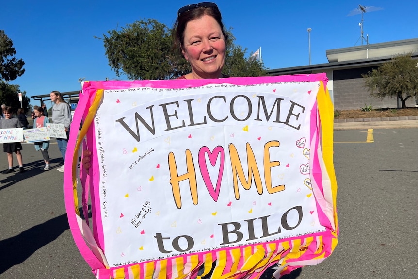 A smiling woman holding a large "welcome" sign at an airport.