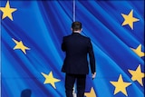A man in a suit walks toward double doors emblazoned with the EU flag.