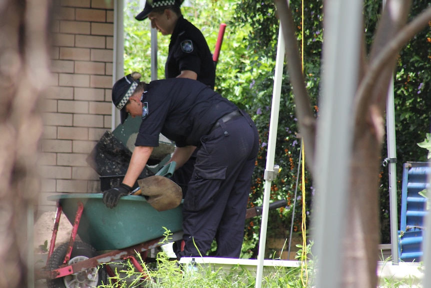 Two police officer stand over a wheelbarrow in a backyard in North Mackay. 