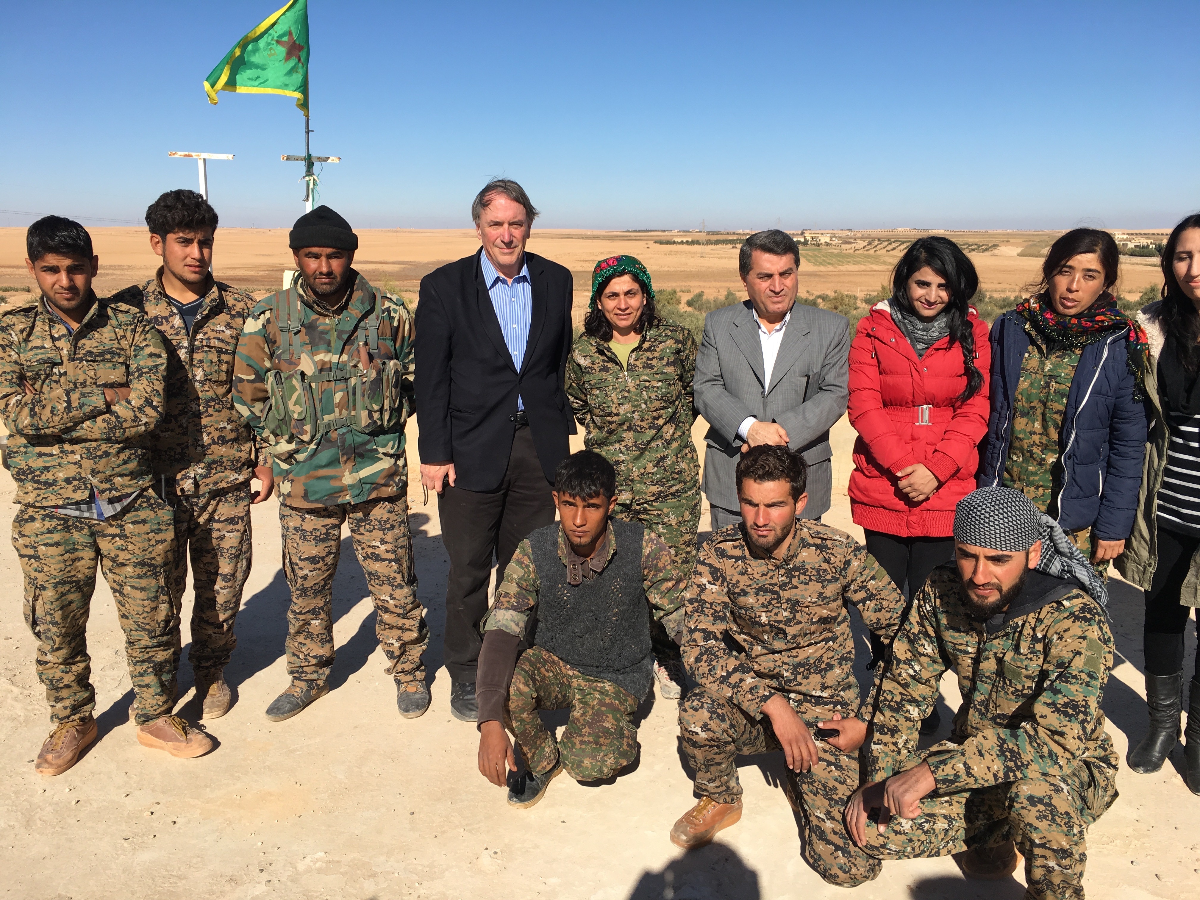 Men and women in army uniform stand beside a suited ambassador.