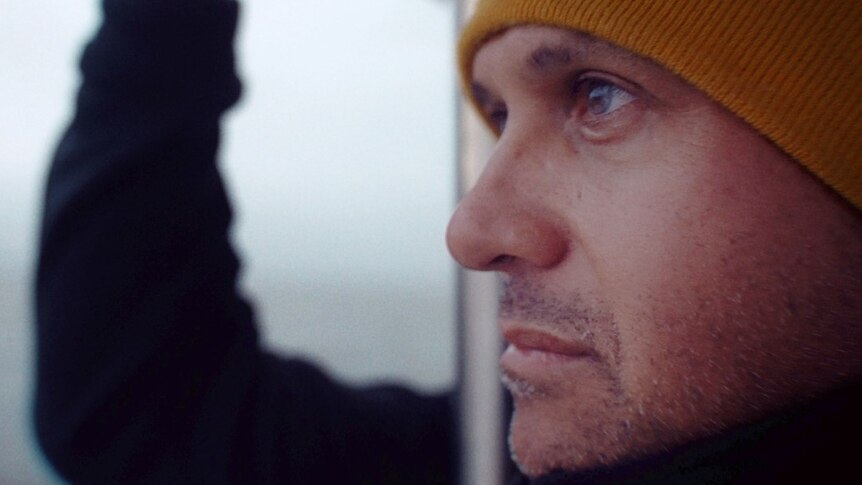 A man's face seen side on, he's wearing a yellow beanie