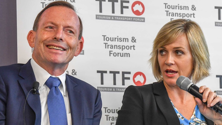 Tony Abbott smiles as Zali Steggall speaks into a microphone at the Warringah candidates' forum.