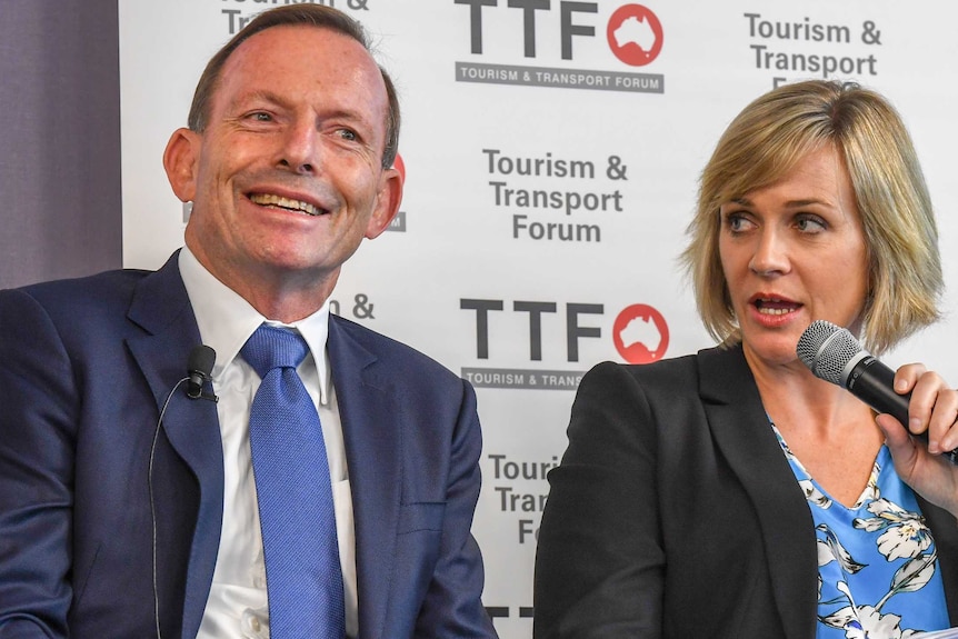 Tony Abbott smiles as Zali Steggall speaks into a microphone at the Warringah candidates' forum.