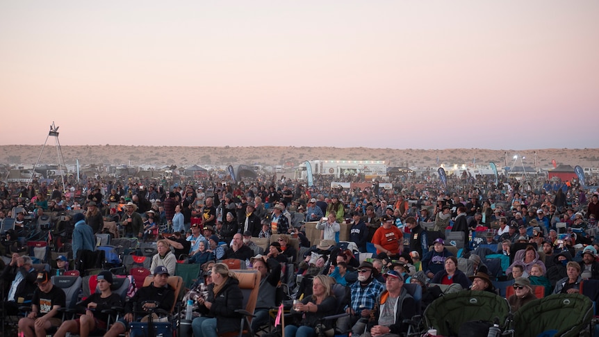 Thousands of people sit on the sand next to the Big Red Sand dune near Birdsville for the 2019 Big Red Bash music festival.