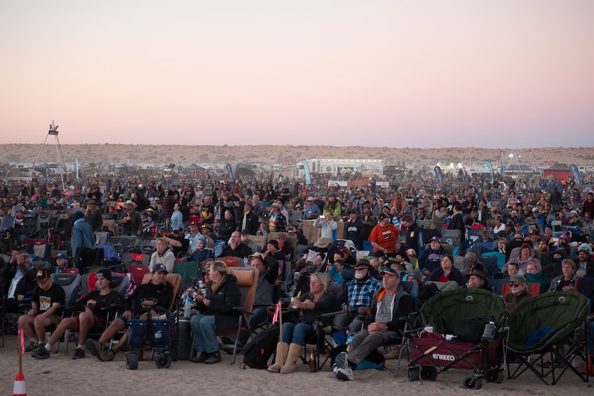 Thousands of people sit on the sand next to the Big Red Sand dune near Birdsville for the 2019 Big Red Bash music festival.