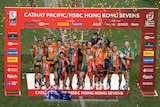 A group of players stand with streamers and confetti around them holding a trophy with a red advertising board around them
