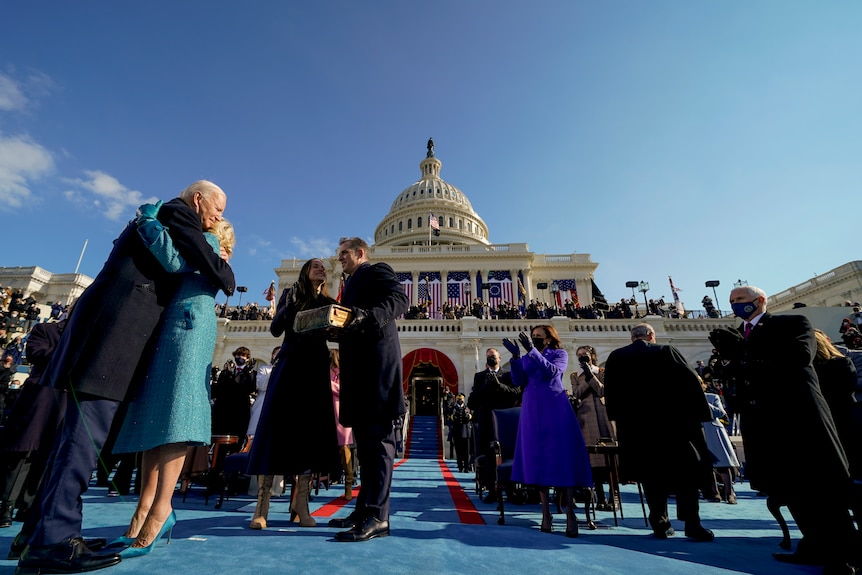 Joe and Jill Biden embrace in front of a crowd of dignitaries.