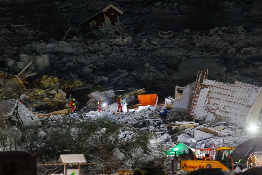 Rescue workers search for signs of life in the rubble caused by the landslide. It is snowy and there is debris all around them.