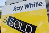 Sold sticker across real estate sign outside house