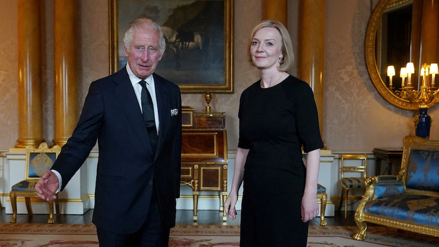 King Charles and Liz Truss, both dressed in black, stand together in a grand room