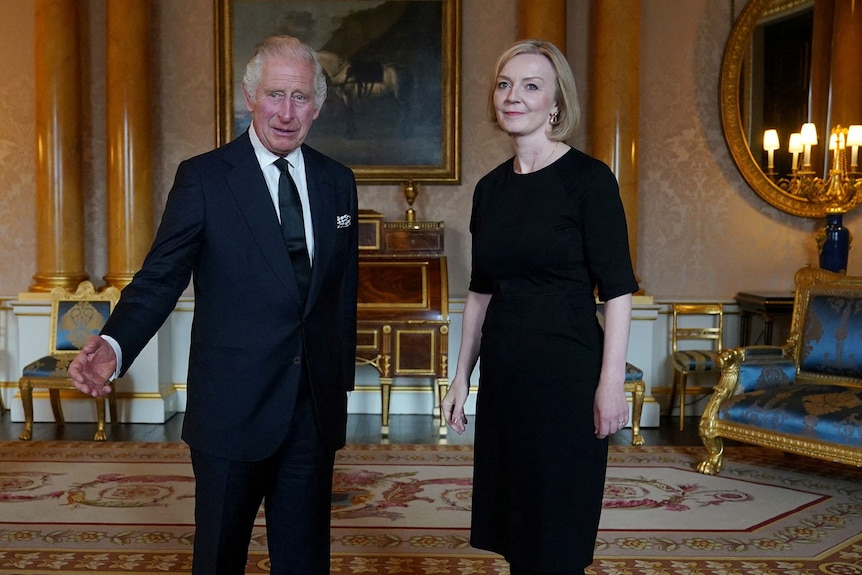 King Charles and Liz Truss, both dressed in black, stand together in a grand room