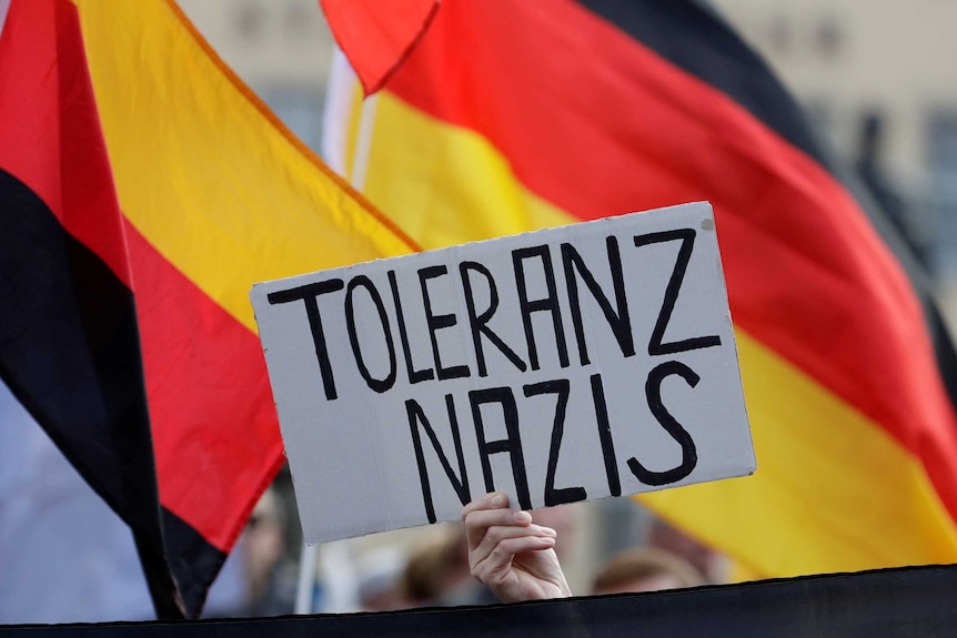 A sign in Germany that translates to "tolerate Nazis" is held up in front of the German flag