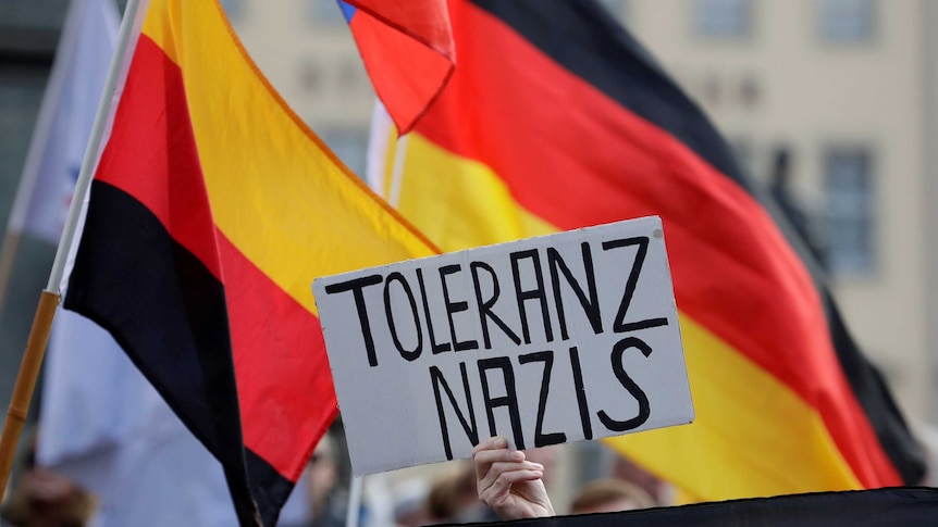 A sign in Germany that translates to "tolerate Nazis" is held up in front of the German flag