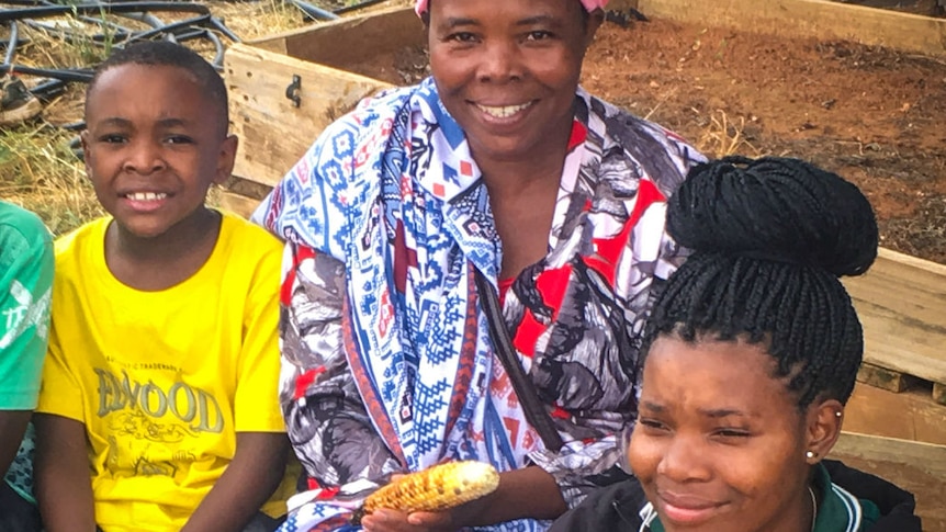 An African woman sits with two of her children eating a piece of cooked maize.