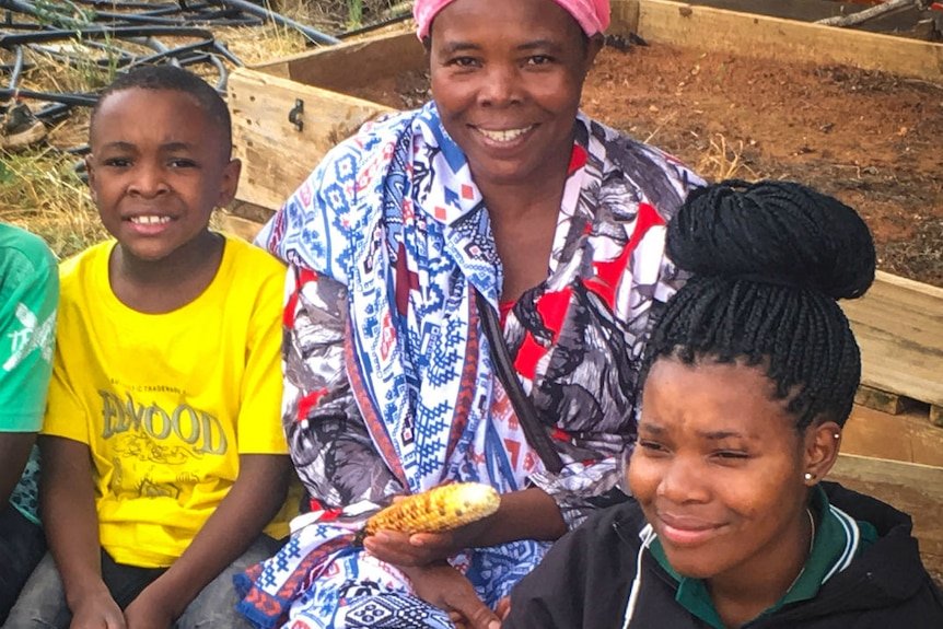 An African woman sits with two of her children eating a piece of cooked maize.