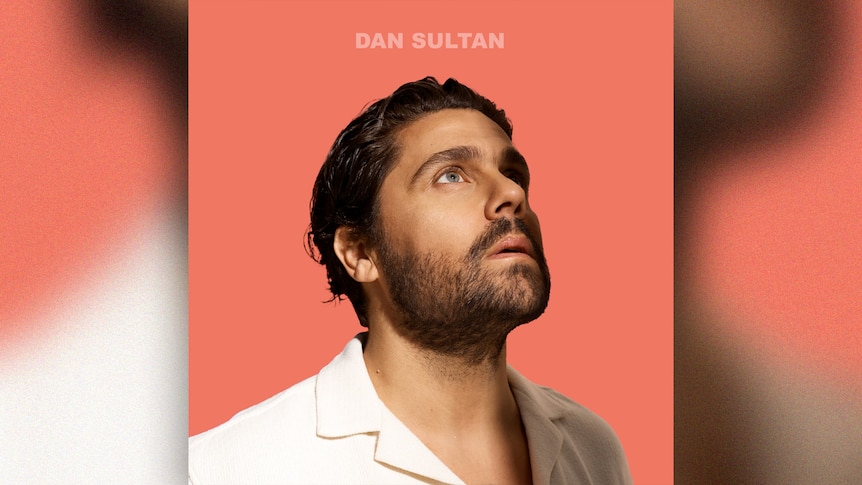 Dan SUltan looks up to the sky wearing a white shirt against an apricot background