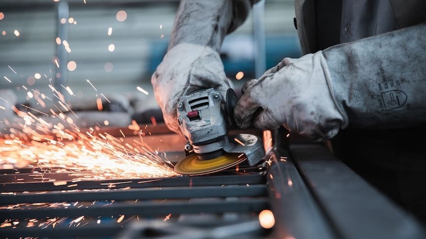 Photo of metal worker, operating a tool and there are sparks flying off it