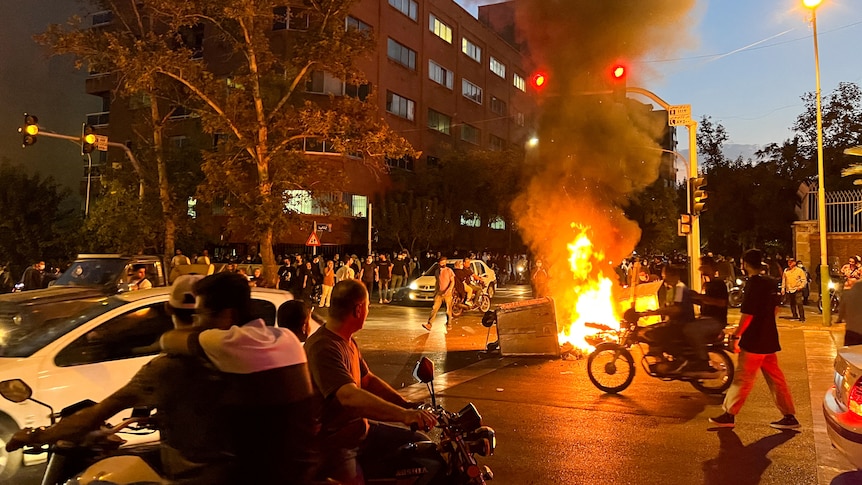 A police motorcycle burns in the street during a protest over the death of Mahsa Amini.