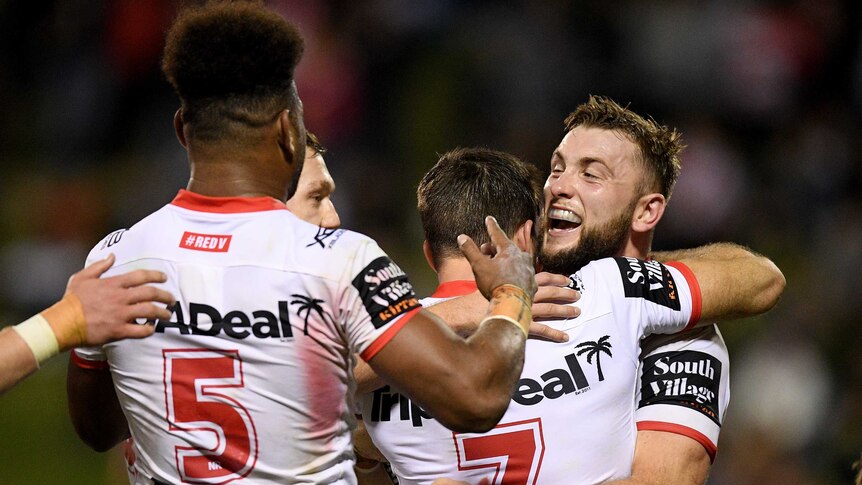Teammates hug an NRL player who has just scored a try.