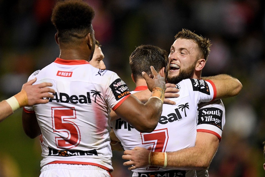 Teammates hug an NRL player who has just scored a try.