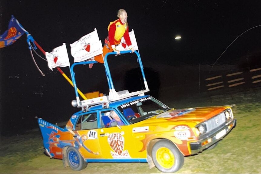 A man balances on top of a rally car.