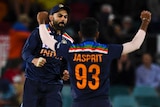 Two Indian male cricketers celebrate in the background as an Australia batter walks off the field.