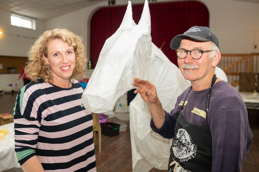 Male and female smiling standing next to a white lantern in the shape of a horse. 