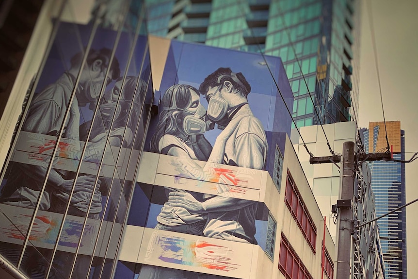 Street art of a couple wearing face masks on a Melbourne building in the CBD with skyscrapers surrounding.