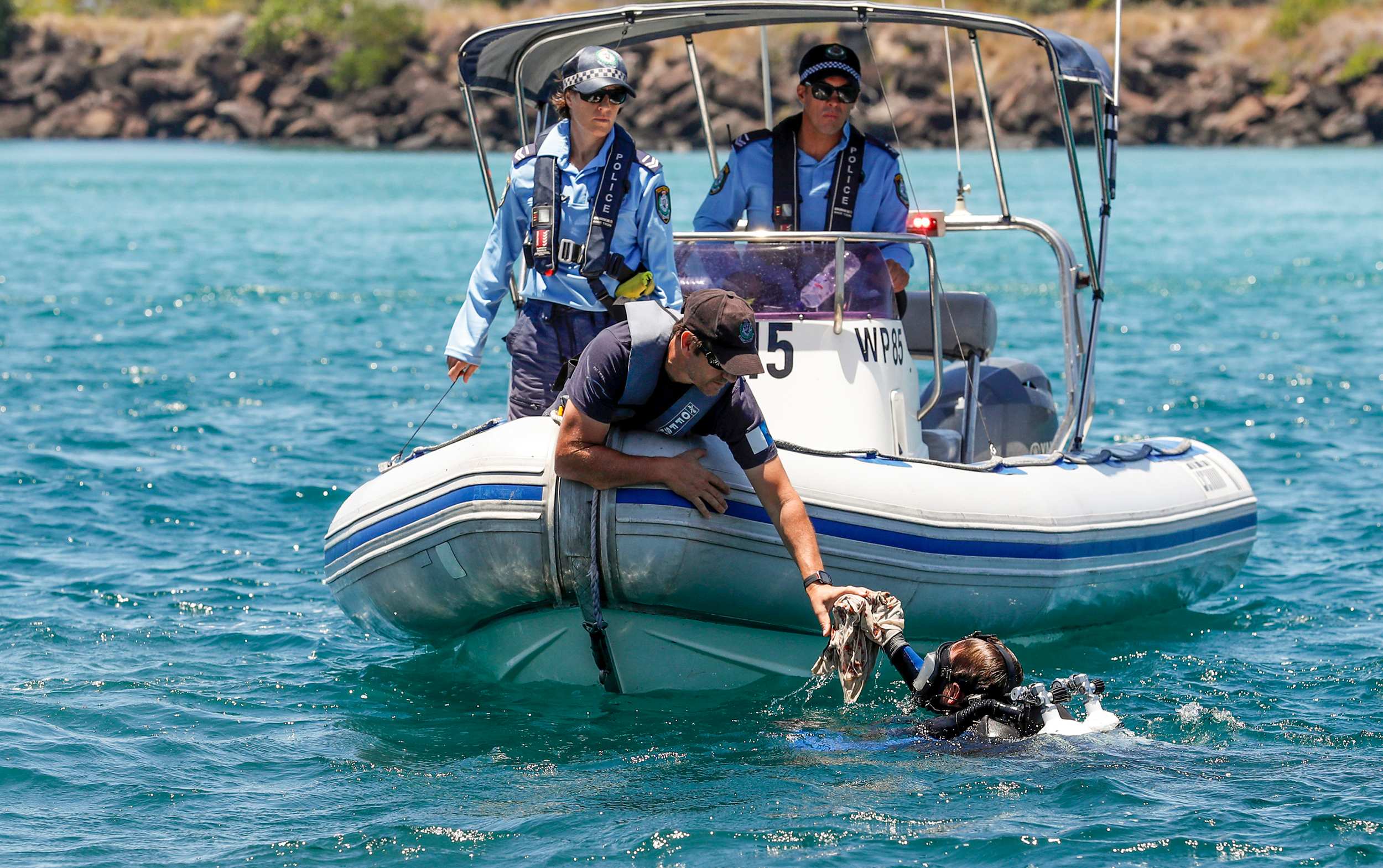 An object is handed to a police officer from a police diver searching the seabed along the Tweed River.